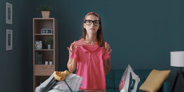 Disappointed housewife having laundry problems, she is holding a shrunken t-shirt - Photo, Image