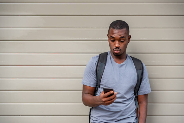 Afro mladý muž pomocí mobilního telefonu u zdi - Fotografie, Obrázek