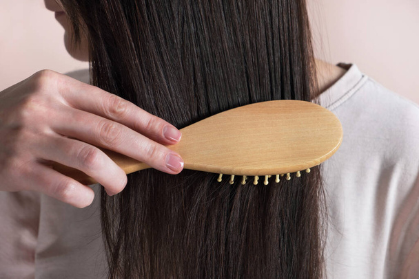 Frau kämmt lange Haare auf pastellbeigem Hintergrund. Gesundes Haar, Pflegekonzept. Nahaufnahme - Foto, Bild