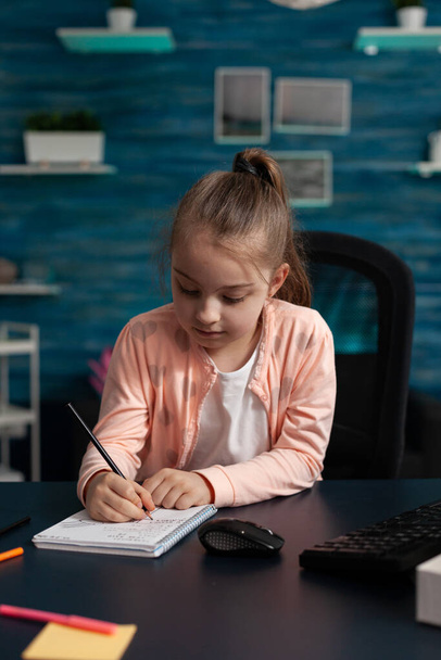 Little schoolchild sitting at desk table in living room writing mathematics exercices - Photo, Image