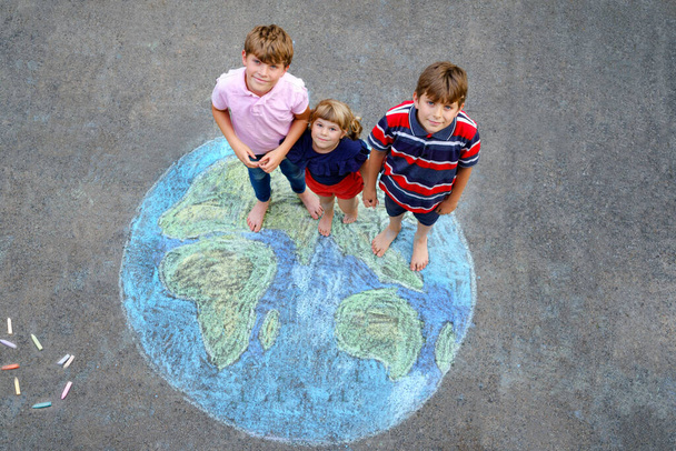 Niña preescolar y dos niños de la escuela con la pintura globo de tierra con tiza de colores en el suelo. Feliz concepto del día de la tierra. Creación de niños para salvar el mundo, el medio ambiente y la ecología. - Foto, Imagen