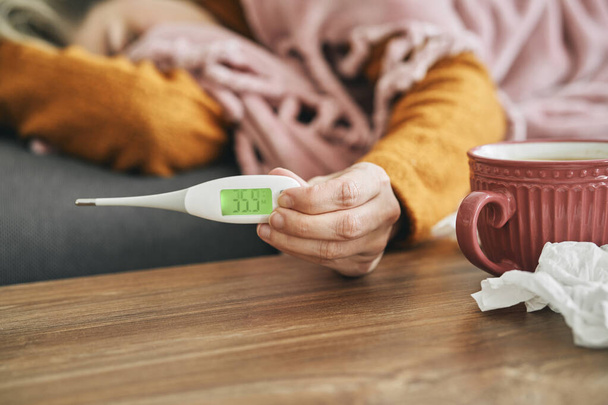 Nierozpoznana chora kobieta trzymająca termometr pokazujący jej temperaturę - Zdjęcie, obraz