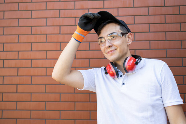 Portret van een jonge man met beschermende koptelefoon en bril op een bakstenen muur achtergrond - Foto, afbeelding