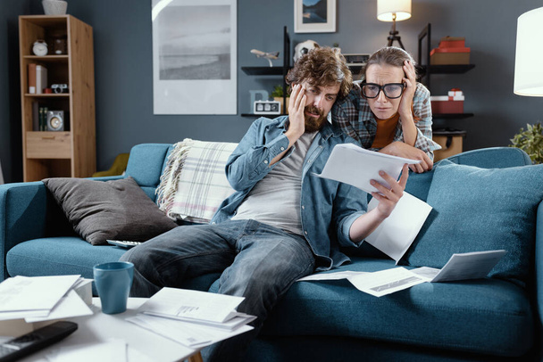 Sad young couple in the living room checking their bills, household budgeting problems concept - Foto, Imagem