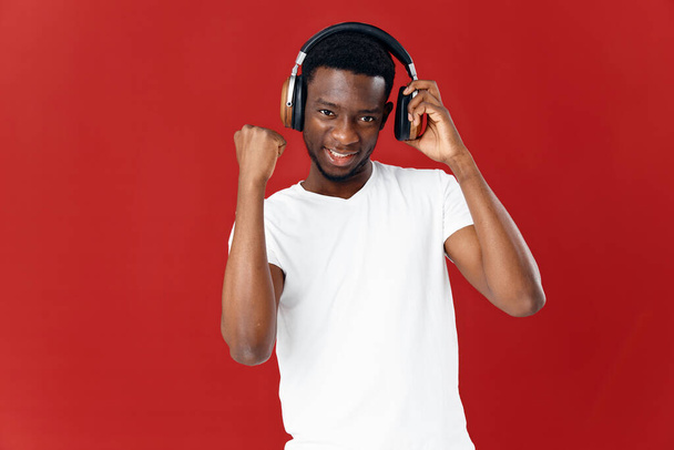 Hombre alegre con auriculares en una camiseta blanca escuchando música entretenimiento fondo rojo - Foto, Imagen