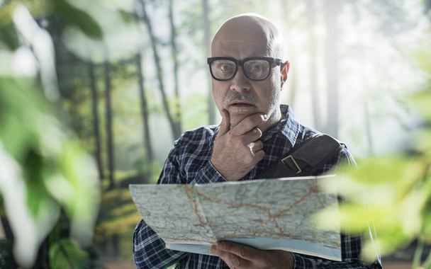Middle aged tourist exploring a forest, he is lost and he is checking a map - Fotó, kép