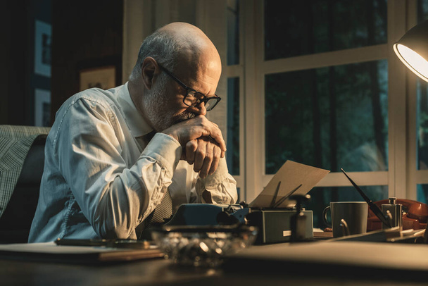 Frustrated writer experiencing a creative slowdown, he is sitting at desk and typing on a vintage typewriter - Fotografie, Obrázek