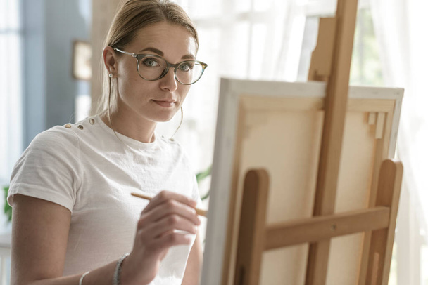 Young beautiful woman painting on canvas in her studio, creativity and hobby concept - 写真・画像
