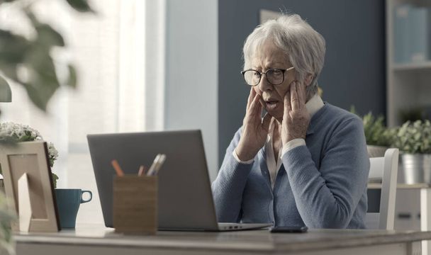 Senior woman struggling with technology, she is confused and staring at the computer screen - Foto, imagen