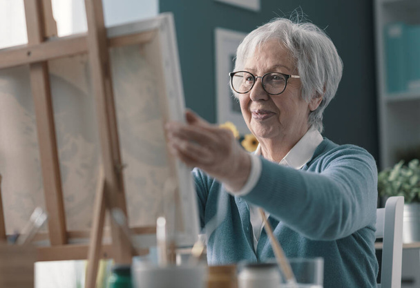 Happy senior woman looking at her finished artwork, hobby and creativity concept - 写真・画像