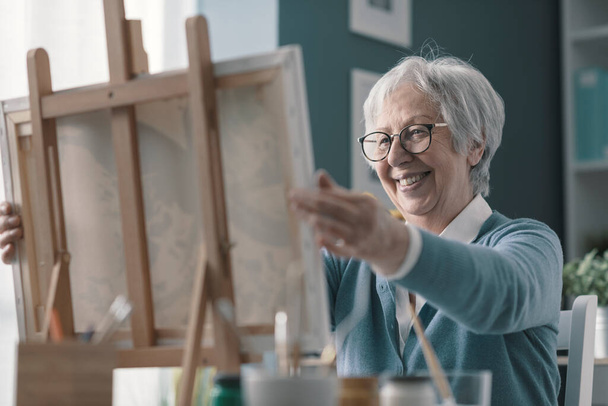 Happy senior woman looking at her finished artwork, hobby and creativity concept - Photo, image