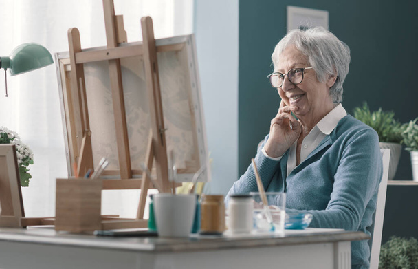 Happy senior woman looking at her finished artwork, hobby and creativity concept - Foto, imagen