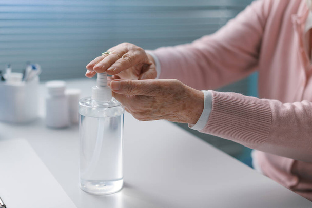 Senior woman applying sanitizer on her hands and wearing a face mask, coronavirus prevention - Фото, изображение