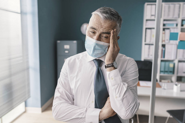 Businessman wearing a face mask, he is having a bad headache, coronavirus covid-19 symptoms - Фото, зображення