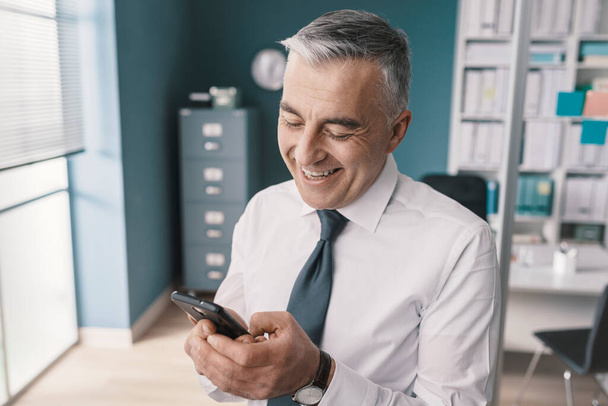 Smiling corporate businessman connecting online using his smartphone - Foto, imagen