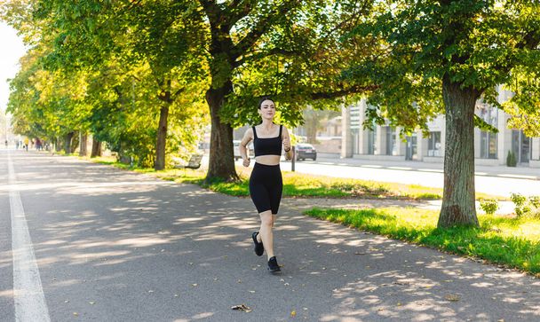 Atlética joven feliz mujer corriendo en el parque corriendo por la mañana para la salud estilo de vida. Entrenamiento al aire libre. Concepto de deporte y estilo de vida activo saludable. - Foto, Imagen