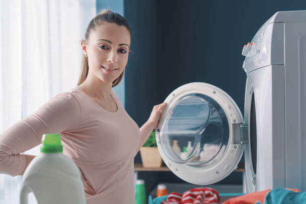 Happy woman doing laundry at home, she is loading the washing machine - Foto, Imagen