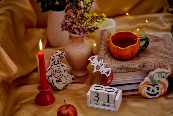 Halloween decorations: candles, homemade cookies, vintage calendar, vase with dry flowers, books, cozy celebrating atmosphere. Autumn Halloween holidays mood. High quality photo - Photo, Image