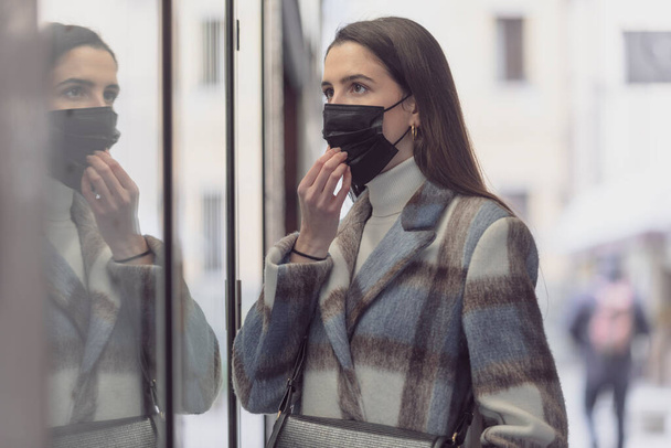 Young woman wearing a protective face mask and looking at the shop window - Foto, immagini