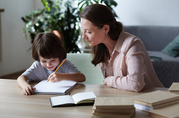 Mom attentively teaches and explains how to complete homework, count, and solve problems - Foto, imagen