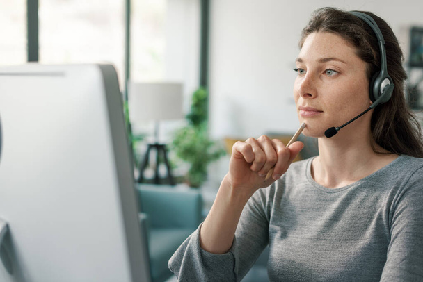 Professional woman sitting at desk, she is wearing a headset and working with her computer - Photo, Image