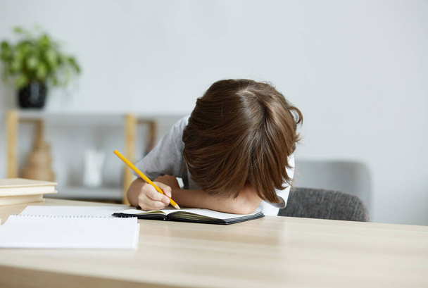 A kimerült iskolás gyerek belefáradt a házi feladatba és a tanulásba, és az asztalon fekszik.. - Fotó, kép