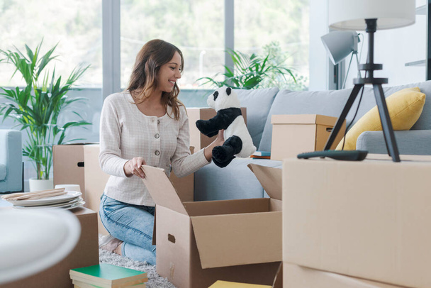 Happy woman unpacking in her new house, she is taking her belongings out of cardboard boxes - Fotoğraf, Görsel