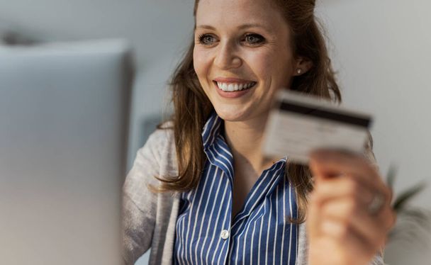 Woman doing online shopping, she is connecting with her laptop and using a credit card - Photo, Image