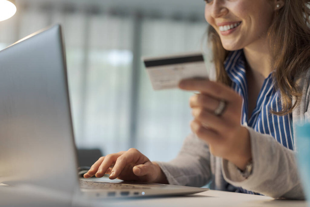 Woman doing online shopping, she is connecting with her laptop and using a credit card - Photo, Image