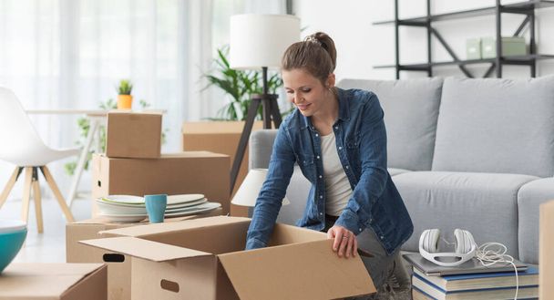 Young happy woman doing a home relocation, she is unpacking in the living room - Фото, изображение