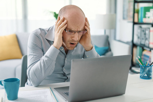 Stressed man working from home, he is shocked and looking at the laptop screen - Foto, Bild