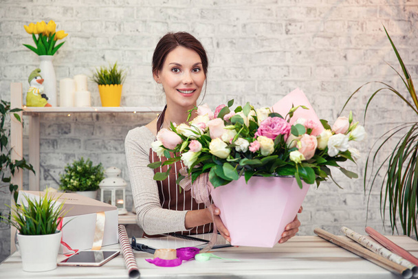 Молодая женщина флорист на работе. Бизнес-леди по продаже и флористике - счастливая улыбчивая женщина, делающая букет в цветочном магазине. Красивая девушка флористка с цветами. Женщина-флористка работает из дома - Фото, изображение