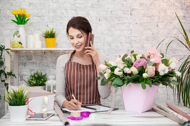 Young woman florist at work. Business woman sale and floristry concept happy smiling woman making bunch at flower shop. Beautiful girl florist with flowers. Female florist working in from home - 写真・画像