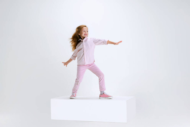 Full-length portrait of smiling girl in casual clothes standing on big box isolated on white studio background. Happy childhood concept. - Foto, immagini