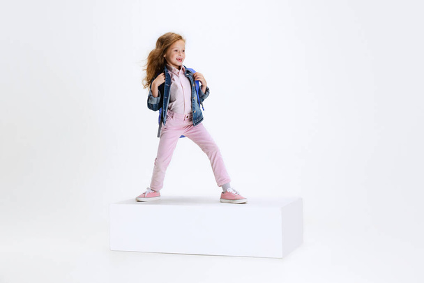 Full-length portrait of smiling girl in casual clothes standing on big box isolated on white studio background. Happy childhood concept. - Φωτογραφία, εικόνα