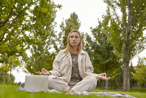 蓮のポーズで座っていた女、足の姿勢を横切った女(スハサナ)と公園で瞑想。魅力的な女性は公園で瞑想することでストレスを軽減します - 写真・画像