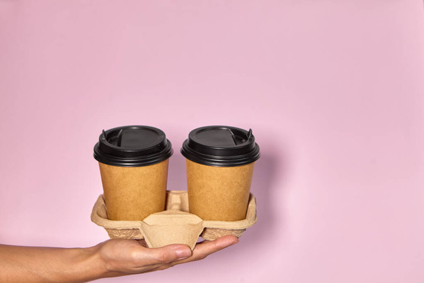 Close-up em um fundo rosa, a mão de uma mulher segura uma xícara de papel com café em um suporte. Café ou chá para levar. Pessoas mãos passando uma outra xícara de café, entrega de café. - Foto, Imagem