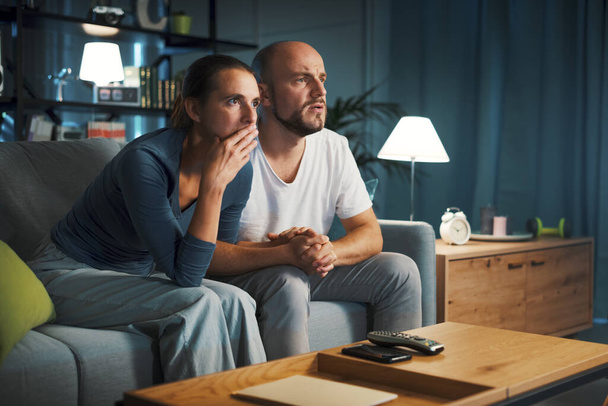 Couple sitting on the couch and watching a drama movie on TV, they are holding hands - Valokuva, kuva