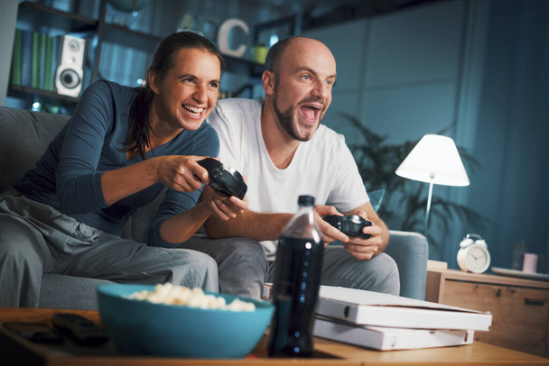 Happy couple spending their weekend at home, they are sitting on the couch and playing video games - Foto, Imagem