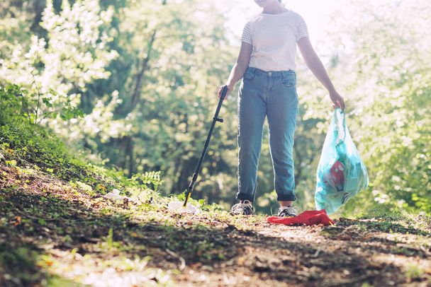 Young girl cleaning up the forest, she is collecting trash and holding a garbage bag, environmental protection concept - Photo, image
