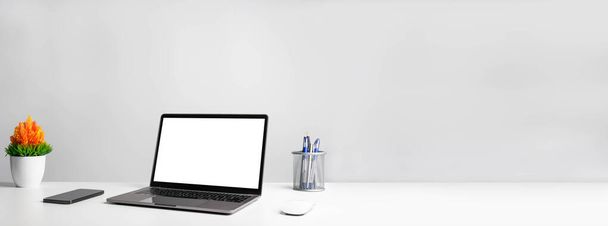 Working concept using technology, notebook, smartphones, devices. Blank white screen laptop on a white table in the office. Copy space on right for design or text, Closeup, Gray, and blur background - Photo, image