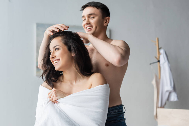 happy shirtless man touching hair of smiling woman wrapped in blanket  - Foto, Bild