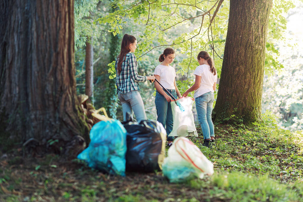 Young volunteers cleaning up the forest, they are putting trash in garbage bags, environmental protection concept - Zdjęcie, obraz