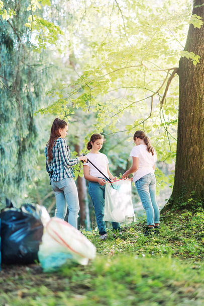 Młodzi wolontariusze sprzątający las, wrzucają śmieci do worków na śmieci, koncepcja ochrony środowiska - Zdjęcie, obraz