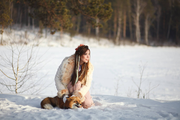 A beautiful girl walks with a fox in a snowy forest. Cold weather. Winter's Tale. Red fox. Photoshoot in a fairy-tale style. - Valokuva, kuva