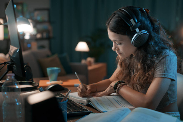 Young student taking online classes at home, she is wearing headphones and watching a video online - Foto, Bild