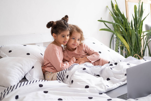 cute little kids girls in pajamas using laptop in bed at home. Kids using technology. - Zdjęcie, obraz