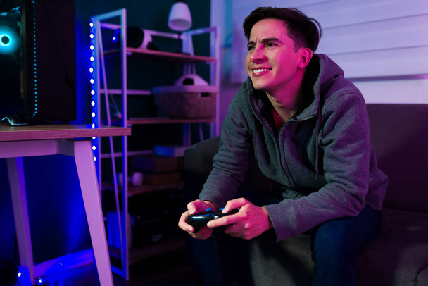 Счастливый кавказский мужчина в свои 20 лет и геймер весело проводит время с экшн-видео-игрой  - Фото, изображение
