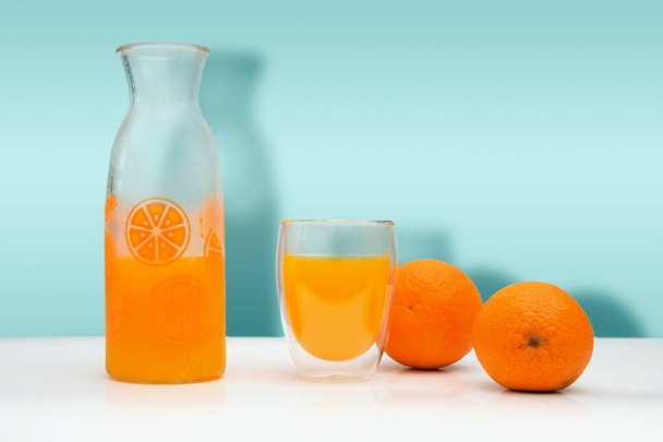 Ripe oranges, a glass bottle and mug with f fresh squeezed orange juice on white background. - Zdjęcie, obraz