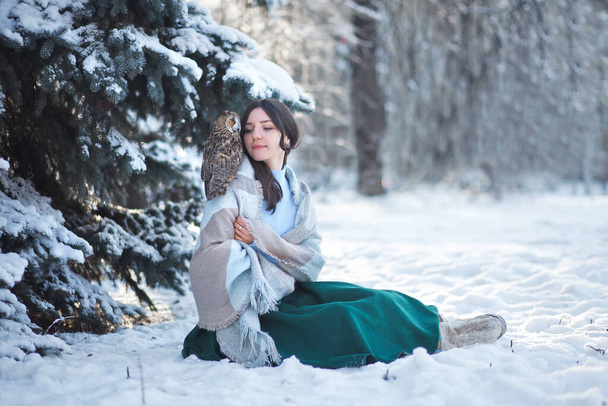Egy gyönyörű lány sétál a téli erdőben egy bagollyal. Művészeti fotózás egy bagollyal. Téli erdő. - Fotó, kép